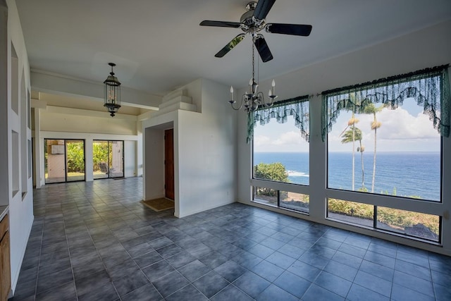 empty room with dark tile patterned floors, ceiling fan with notable chandelier, and a water view