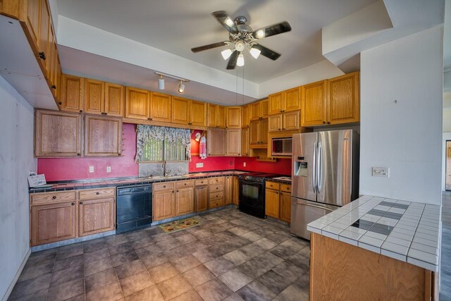 kitchen featuring brown cabinets, black appliances, a ceiling fan, a sink, and tile counters