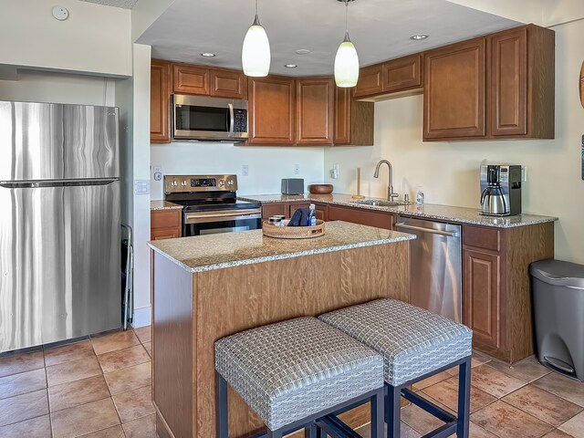 kitchen featuring light stone countertops, stainless steel appliances, a sink, brown cabinets, and a center island