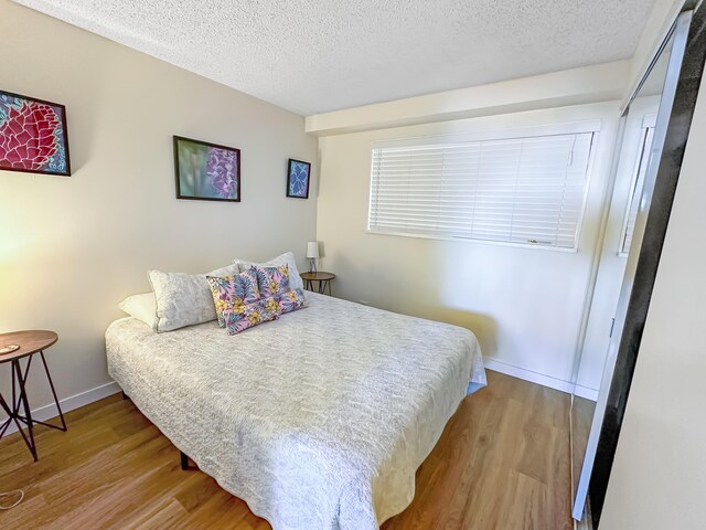 bedroom featuring a textured ceiling, wood finished floors, and baseboards