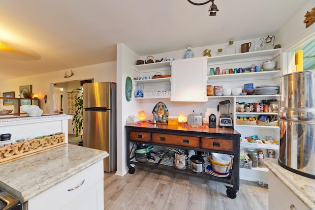 kitchen featuring light stone counters, light hardwood / wood-style flooring, stainless steel refrigerator, and white cabinets