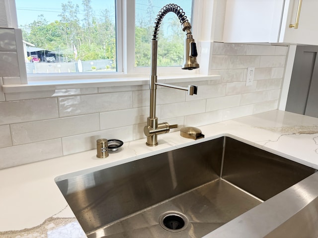 room details with white cabinetry, light stone counters, sink, and tasteful backsplash