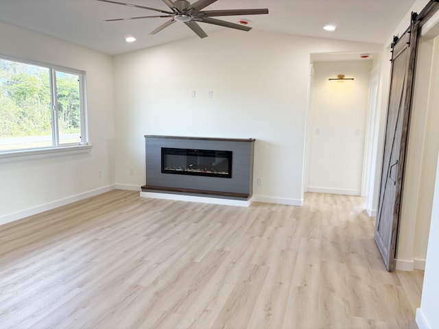 unfurnished living room with lofted ceiling, light hardwood / wood-style flooring, a barn door, and ceiling fan