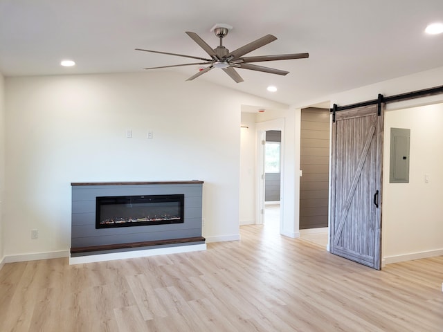 unfurnished living room featuring vaulted ceiling, electric panel, ceiling fan, light hardwood / wood-style floors, and a barn door