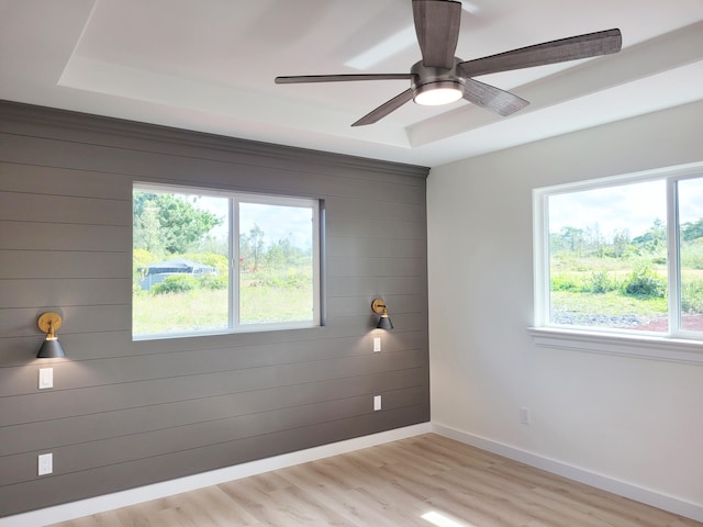 spare room with ceiling fan, wood walls, a raised ceiling, and light wood-type flooring