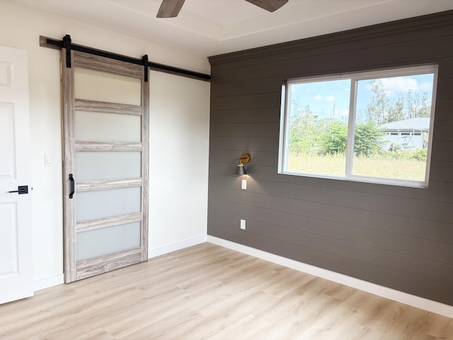 unfurnished bedroom featuring a closet, wooden walls, a barn door, and light wood-type flooring