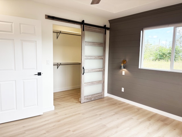 unfurnished bedroom featuring a barn door, wooden walls, light wood-type flooring, and a closet