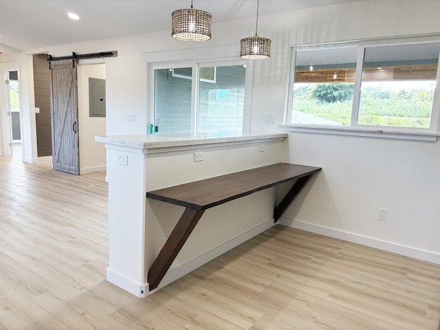 kitchen featuring decorative light fixtures, light hardwood / wood-style flooring, electric panel, and a barn door