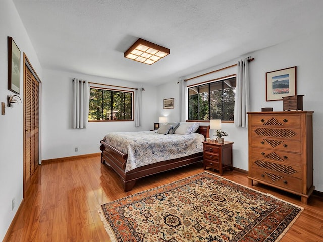 bedroom with light wood-type flooring, a closet, multiple windows, and baseboards