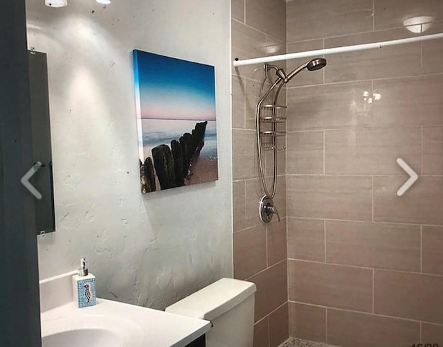 bathroom featuring a tile shower, vanity, and toilet
