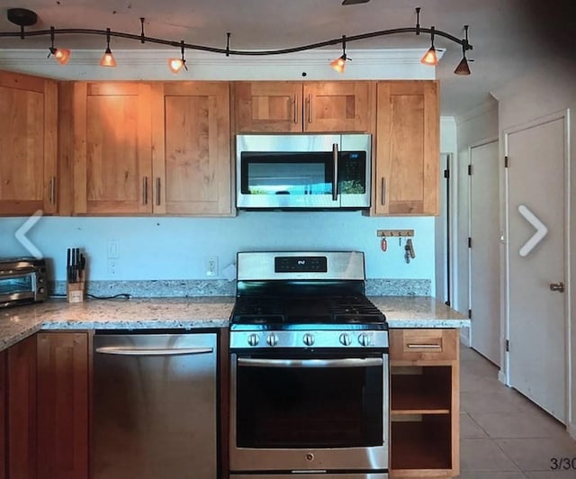 kitchen with light stone countertops, light tile patterned floors, ornamental molding, and stainless steel appliances