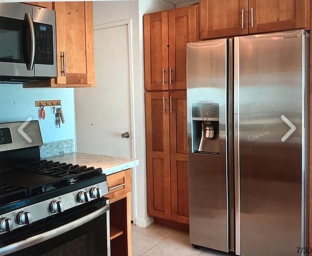 kitchen featuring appliances with stainless steel finishes, light tile patterned floors, and light stone counters