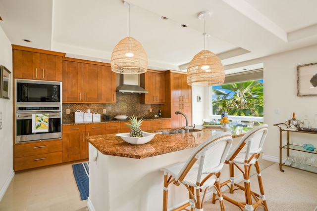 kitchen featuring wall chimney range hood, hanging light fixtures, black appliances, decorative backsplash, and a raised ceiling