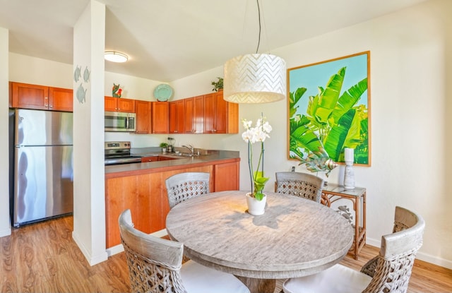 kitchen featuring a sink, baseboards, appliances with stainless steel finishes, light wood-type flooring, and brown cabinetry