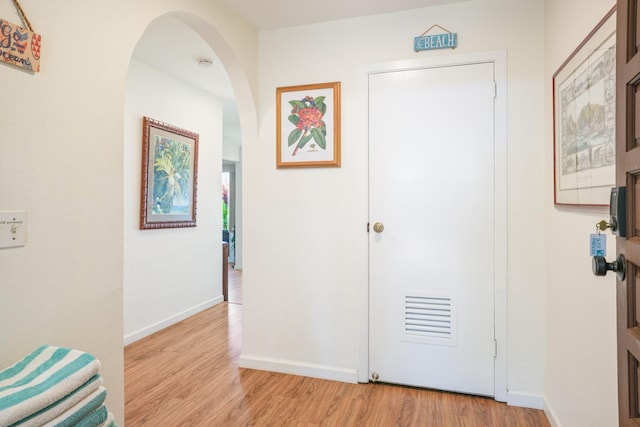 hall with light wood-style floors, arched walkways, and baseboards