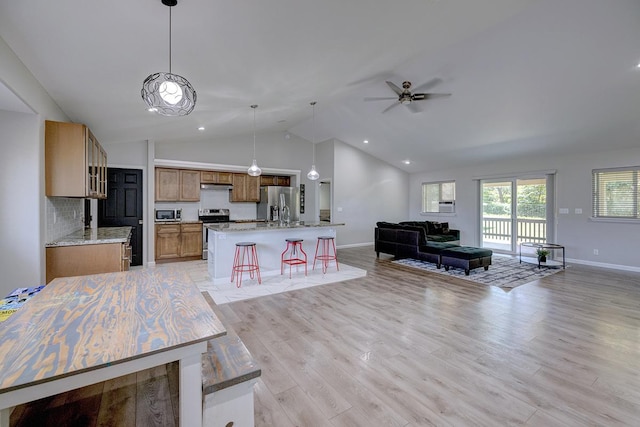 kitchen with pendant lighting, stainless steel appliances, open floor plan, a kitchen island with sink, and light wood-type flooring