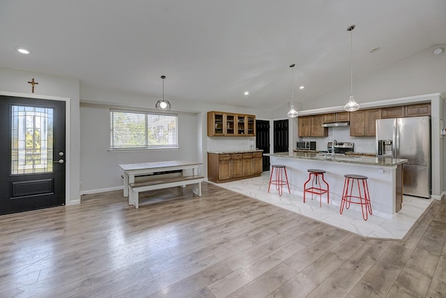 kitchen featuring light wood-style flooring, brown cabinets, a kitchen breakfast bar, stainless steel appliances, and under cabinet range hood