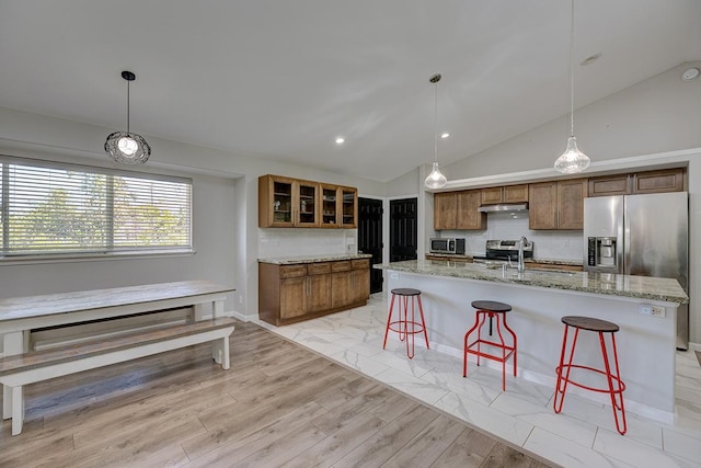 kitchen with a breakfast bar, under cabinet range hood, brown cabinets, and decorative backsplash