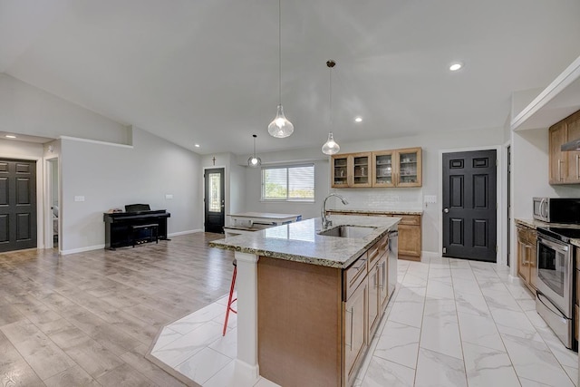 kitchen with lofted ceiling, an island with sink, glass insert cabinets, stainless steel appliances, and a sink