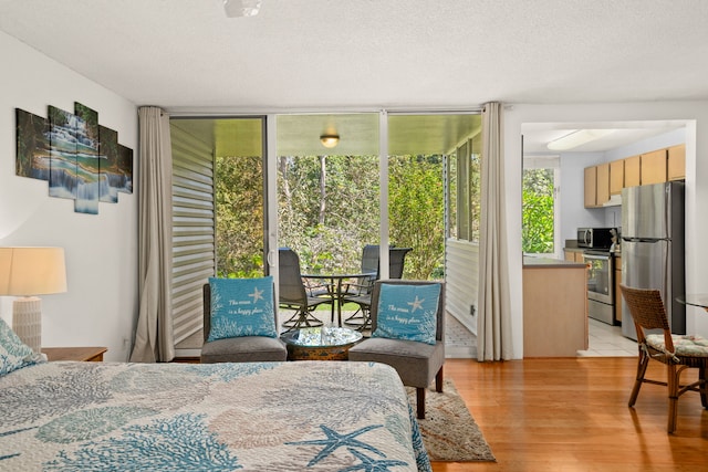 bedroom featuring light wood-type flooring, a wall of windows, stainless steel refrigerator, and a textured ceiling