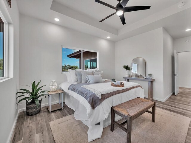 bedroom featuring a tray ceiling, ceiling fan, and light wood-type flooring