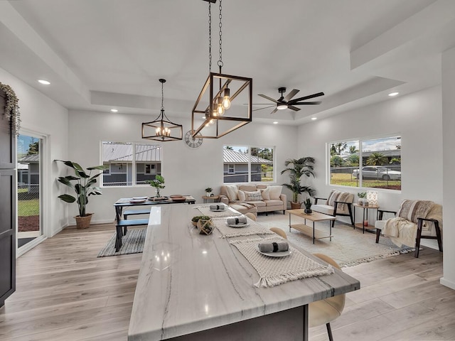 kitchen with decorative light fixtures, light wood-type flooring, a raised ceiling, and light stone countertops