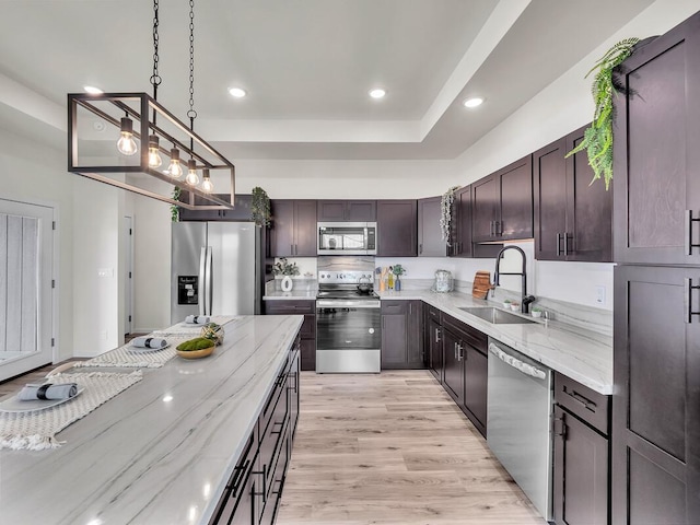 kitchen with decorative light fixtures, stainless steel appliances, light stone counters, and sink