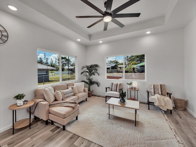 living room with a raised ceiling, a healthy amount of sunlight, ceiling fan, and light wood-type flooring