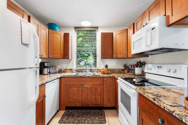 kitchen with sink, white appliances, light tile patterned floors, light stone counters, and a textured ceiling