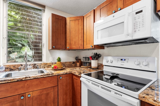 kitchen featuring light stone counters, white appliances, sink, and a textured ceiling