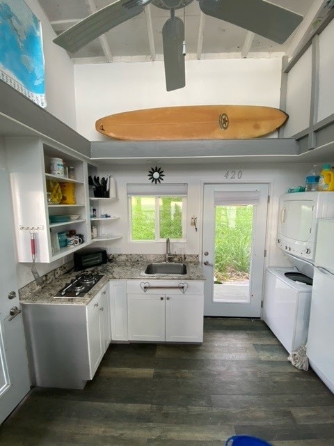 kitchen featuring sink, stacked washer and dryer, white cabinetry, a towering ceiling, and light stone countertops