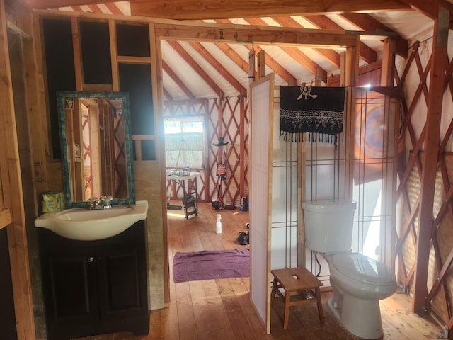 bathroom featuring wood-type flooring, toilet, lofted ceiling with beams, and vanity