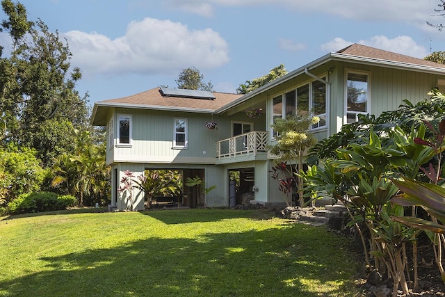 rear view of house with a yard, a balcony, and solar panels