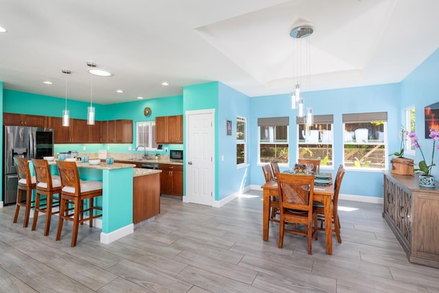 kitchen featuring a center island, brown cabinets, decorative light fixtures, stainless steel appliances, and a raised ceiling