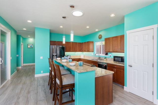 kitchen with brown cabinets, appliances with stainless steel finishes, a kitchen island with sink, a sink, and a kitchen breakfast bar