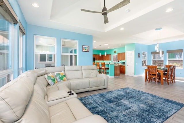 living area with light wood-style floors, a raised ceiling, and recessed lighting