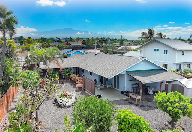 back of property with an outbuilding, roof with shingles, a patio area, fence, and a mountain view