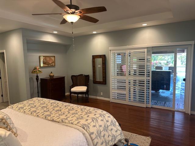 bedroom with dark wood-type flooring, a raised ceiling, ceiling fan, and access to outside