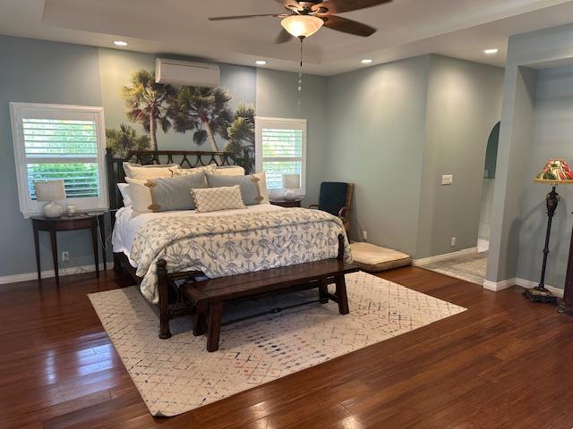 bedroom featuring ceiling fan, dark hardwood / wood-style floors, and a wall unit AC