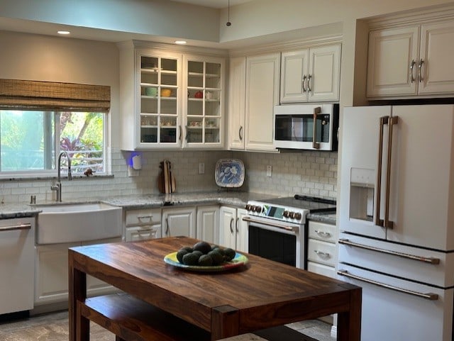 kitchen featuring light stone counters, premium appliances, decorative backsplash, and sink