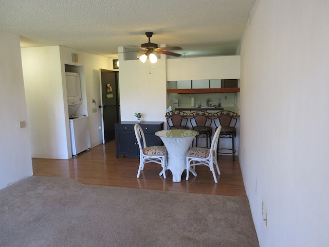 dining area with a textured ceiling, ceiling fan, stacked washer and dryer, carpet floors, and wood finished floors