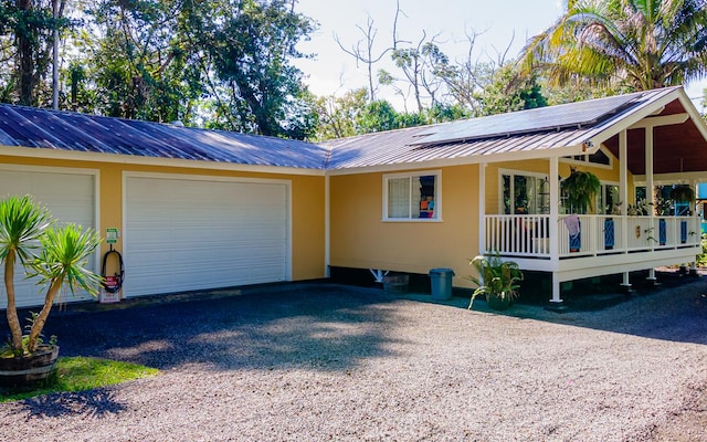 view of front of home featuring metal roof, an attached garage, covered porch, driveway, and roof mounted solar panels