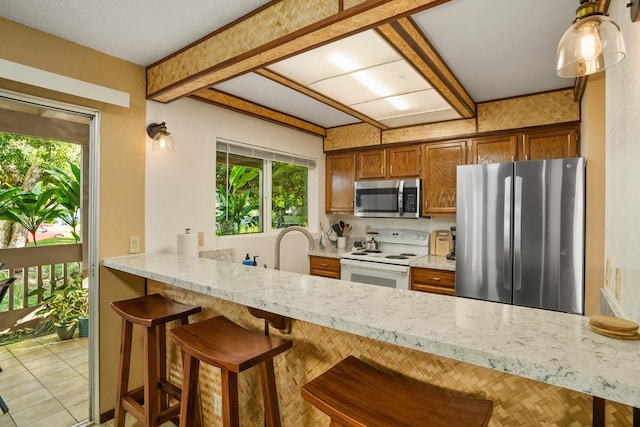 kitchen featuring beam ceiling, appliances with stainless steel finishes, a kitchen bar, and kitchen peninsula