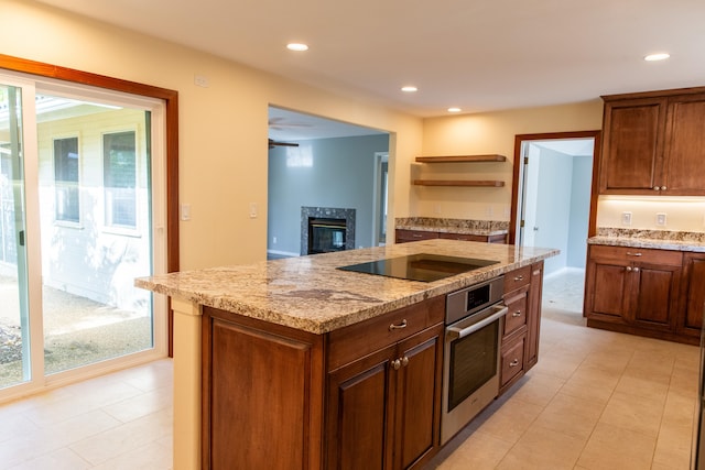 kitchen featuring a center island with sink, a high end fireplace, oven, light stone counters, and black electric stovetop