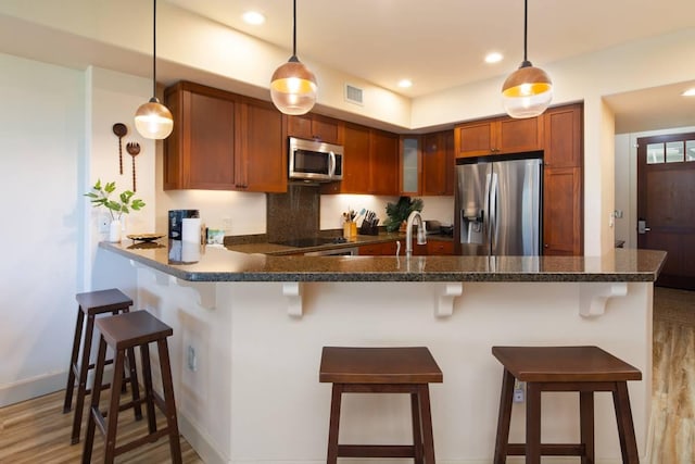 kitchen with appliances with stainless steel finishes, pendant lighting, sink, a kitchen breakfast bar, and kitchen peninsula