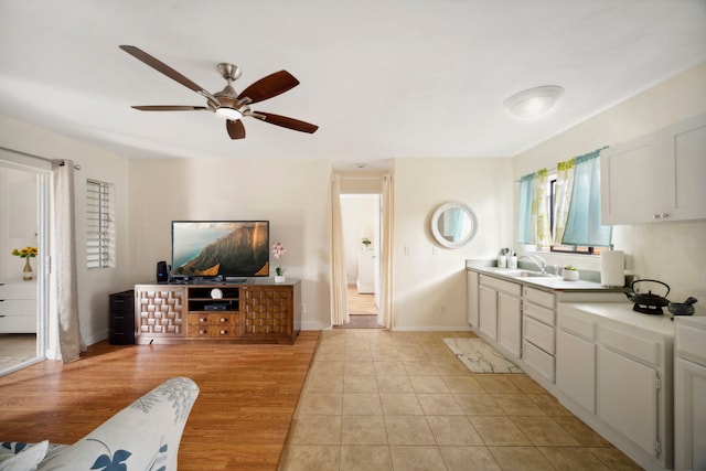 kitchen with a sink, light countertops, a ceiling fan, baseboards, and light tile patterned floors