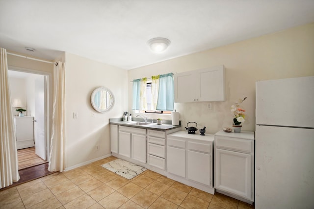 kitchen featuring freestanding refrigerator, white cabinetry, a sink, and light tile patterned floors