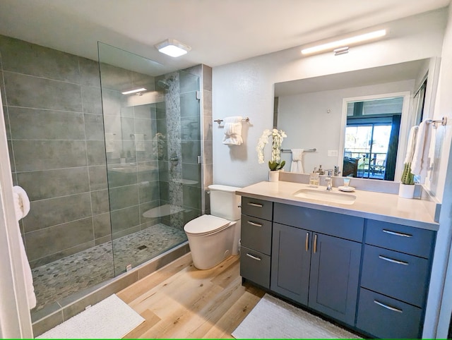 bathroom featuring hardwood / wood-style flooring, vanity, tiled shower, and toilet