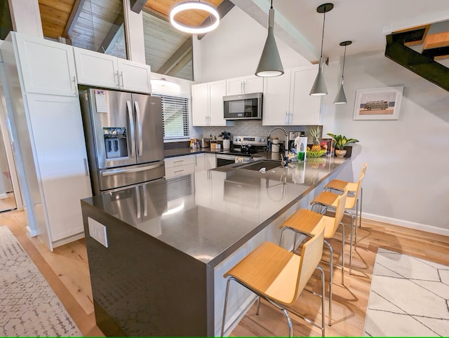 kitchen featuring white cabinetry, stainless steel appliances, kitchen peninsula, hanging light fixtures, and a breakfast bar area