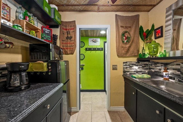 kitchen with light tile patterned floors, a sink, decorative backsplash, open shelves, and dark countertops